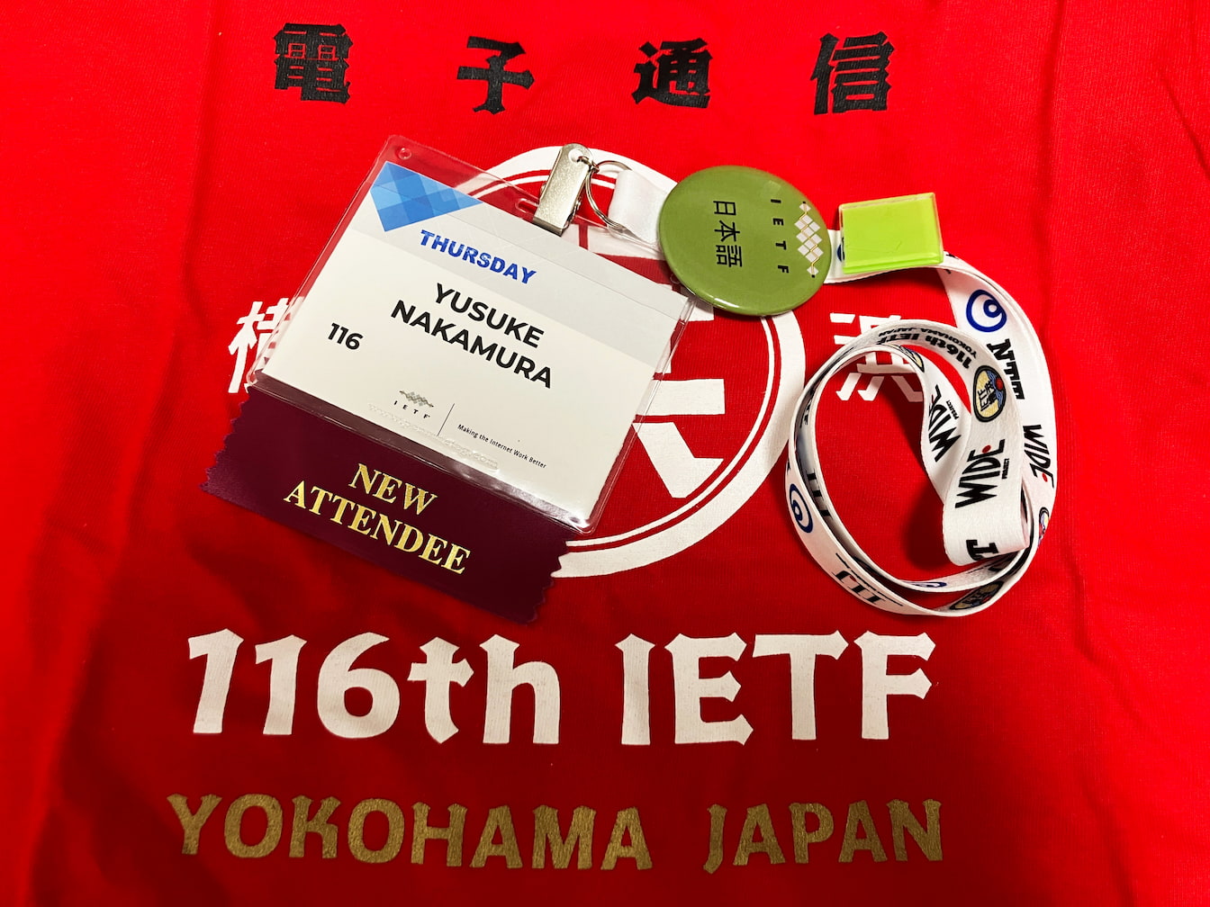 IETF116の参加記念？Tシャツと名札。NEW ATTENDEEのリボンをつけている